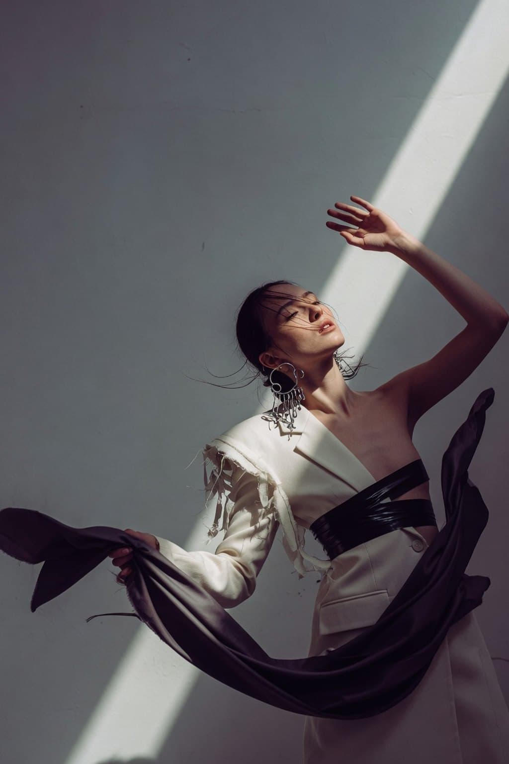 Dark silk caught mid-movement against a raw plaster wall under a hard diagonal of light - rendered by McLeuker AI