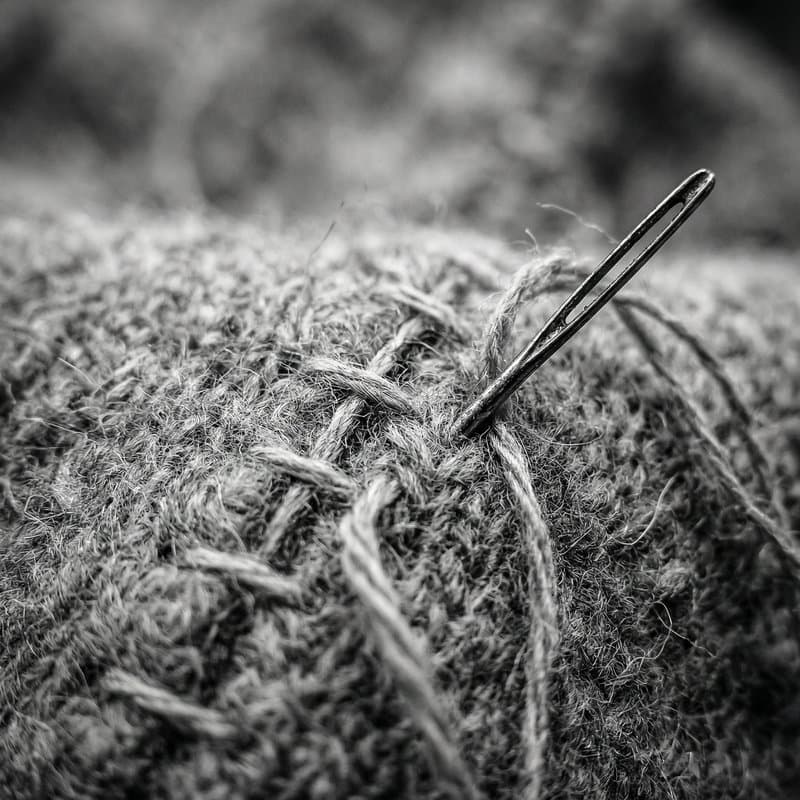 A needle and coarse thread drawn through thick tweed